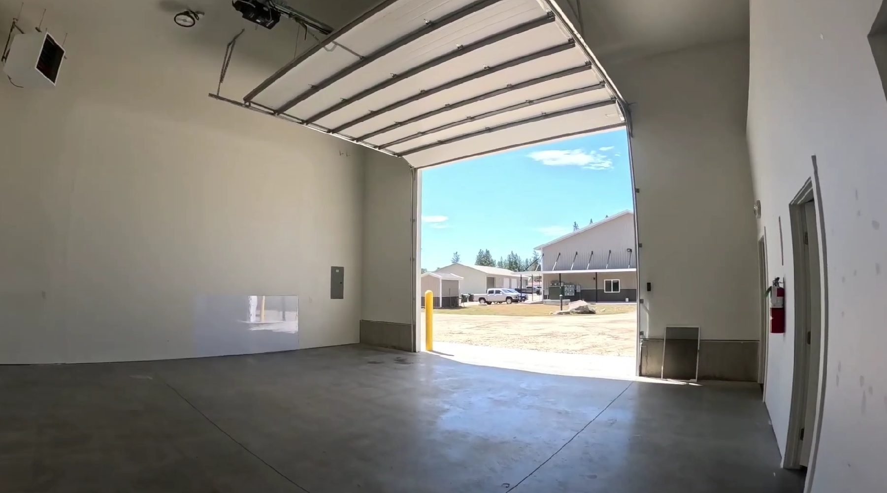 Inside a unit: an open roll-up bay door looking out to the gravel yard, a sealed concrete slab, and a door through to the private office.