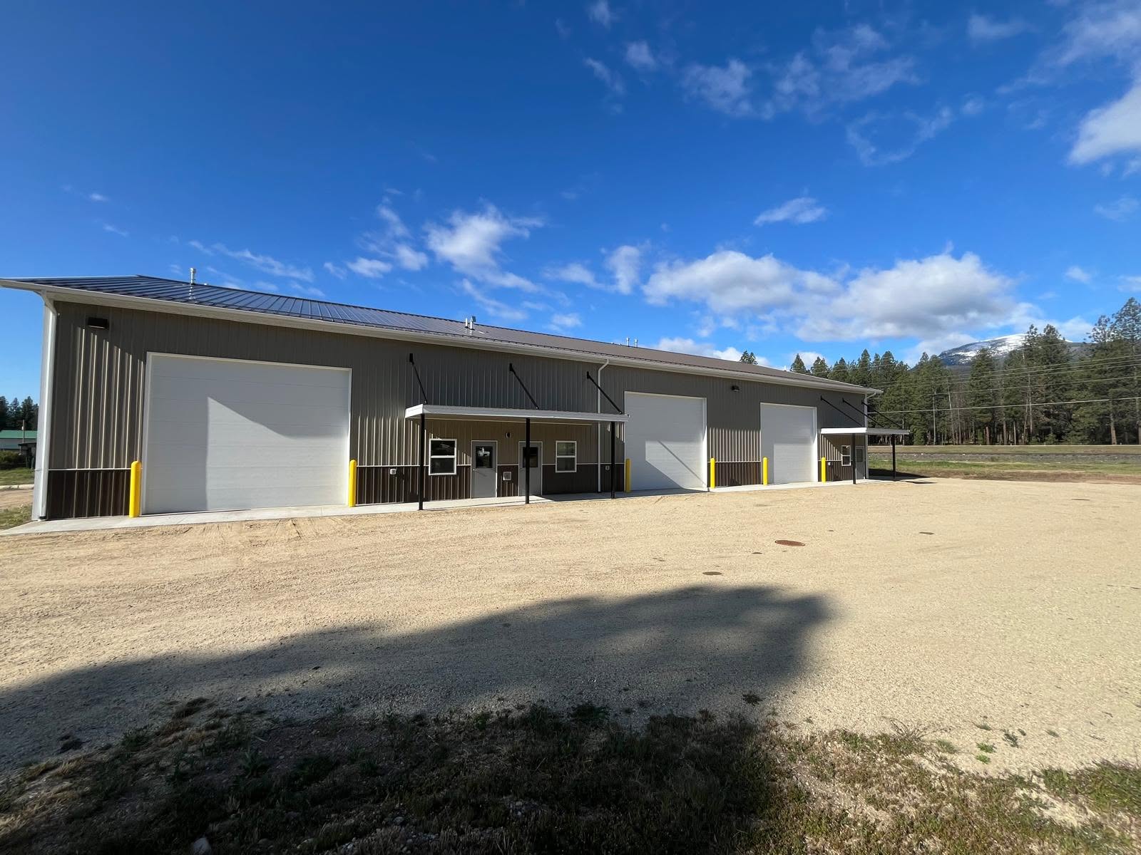 A Bitterroot Industrial flex building with white roll-up bay doors along a gravel apron, the Bitterroot Range behind it.